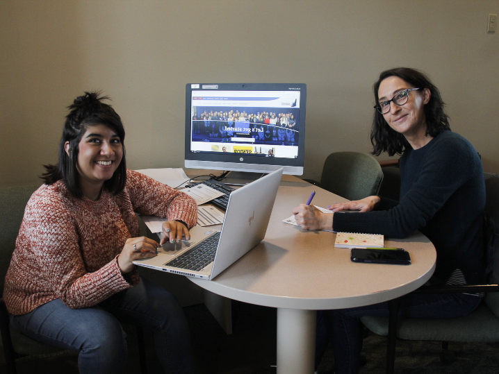 两个学生坐在一张桌子前，一个用笔记本电脑